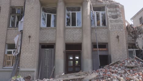 front view of a heavily damaged school building in shelling with collapsed sections and rubble piles