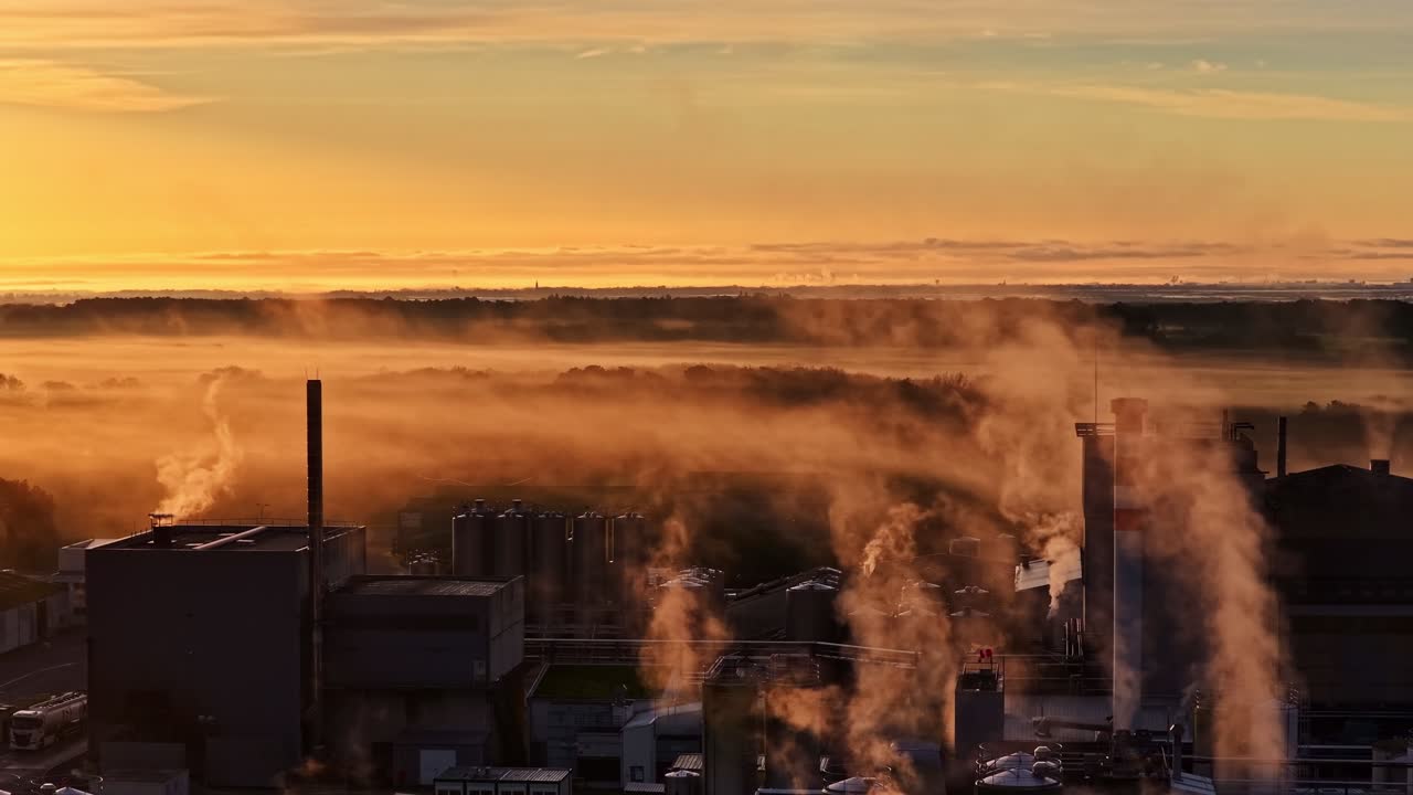Golden sunrise over a smoky industrial factory and rural landscape