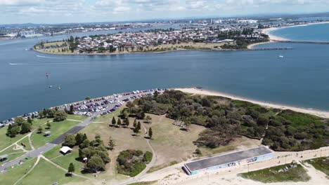 Drone-Volando-Sobre-Un-Parque-Y-Un-Aparcamiento-Hacia-Un-Recodo-De-Un-Río-Y-Una-Gran-Ciudad-Australiana