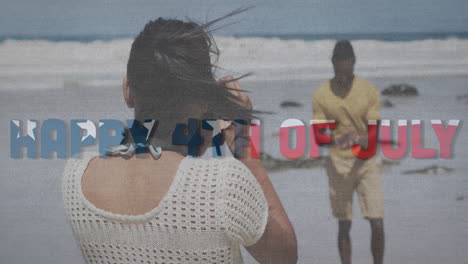 animation of text independence day over african american couple taking photo at beach