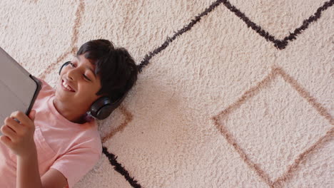 lying on carpet, boy wearing headphones using tablet, smiling and relaxed, copy space