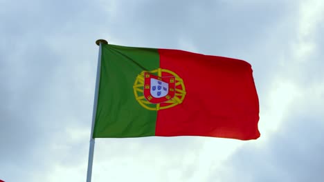 portugal portuguese bandeira das quinas flag waving in wind in slow motion with sunny blue sky clouds background