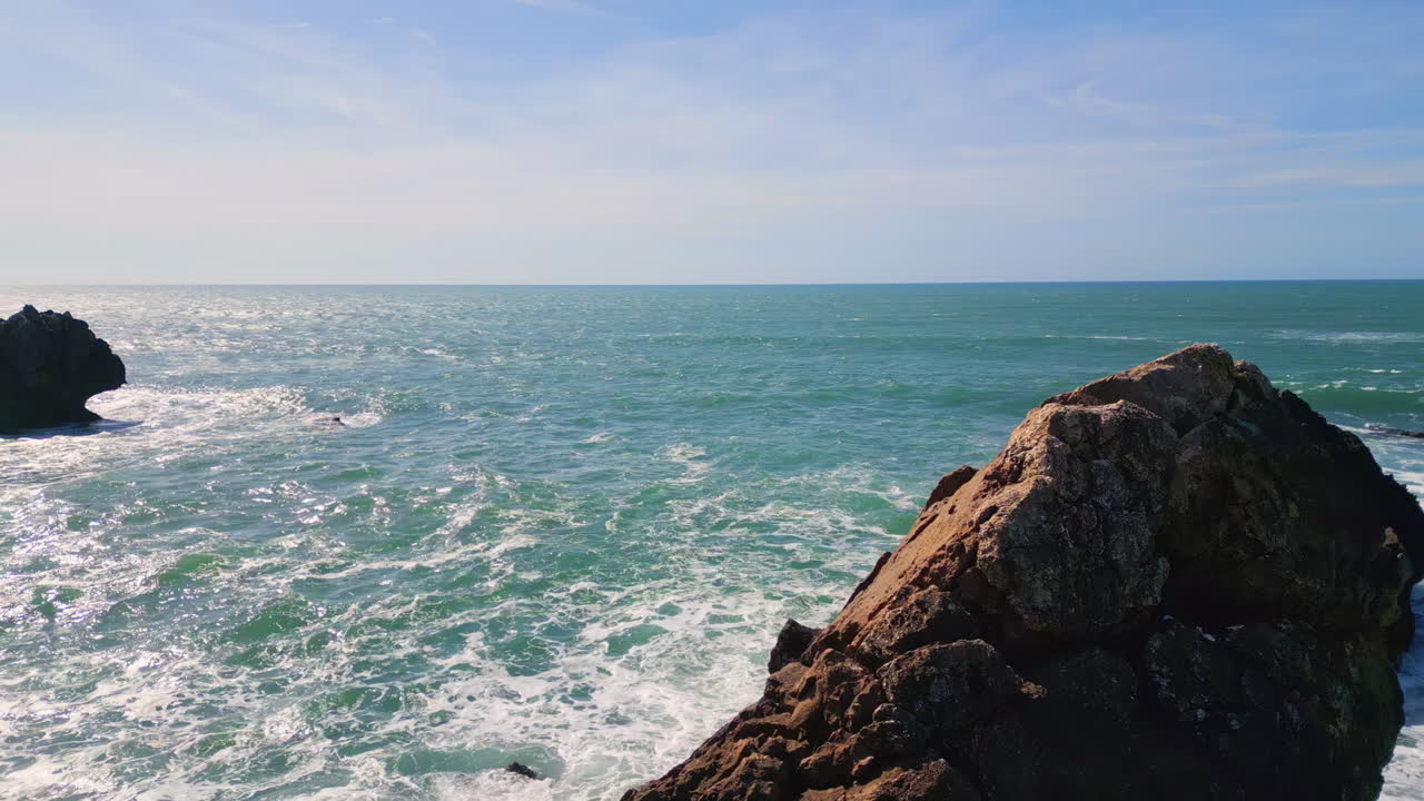 Drone breathtaking endless ocean surface sparkling under sunlight. Rocky coast