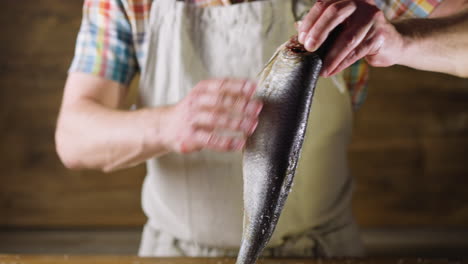 man in apron removes salt from tasty fat marinated herring