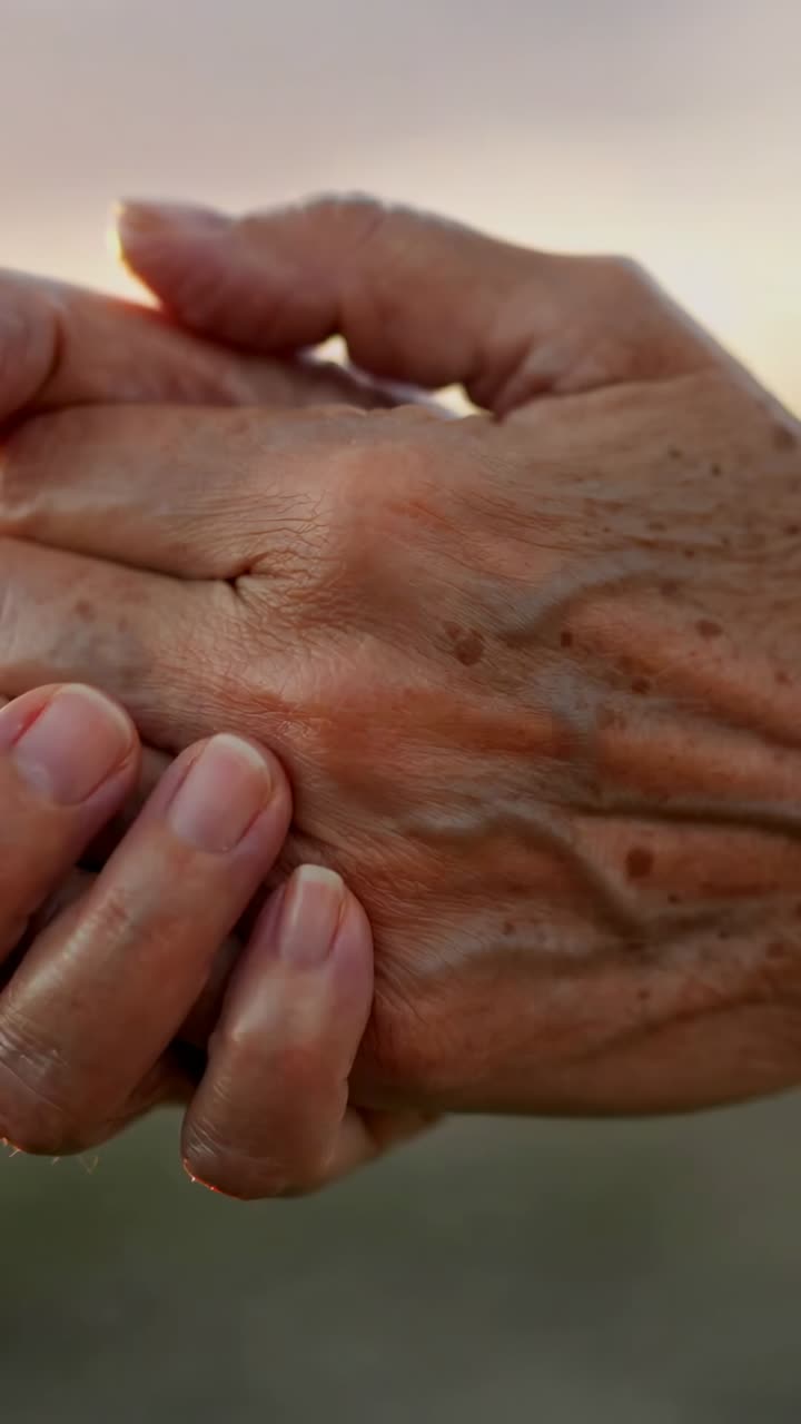 Vertical video: Placing adult hand on senior hand at sunset pressing and sliding fingers comforting
