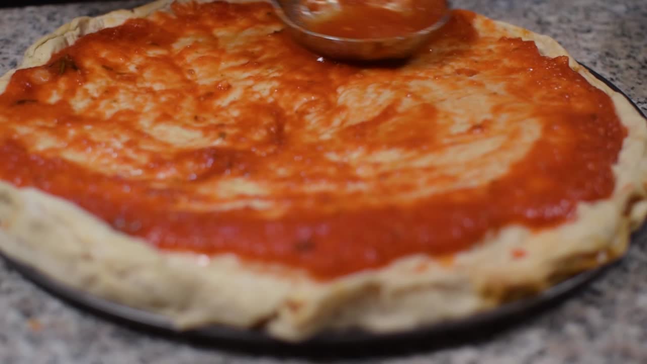 Chef che applica e spalma la salsiccia su una pizza con un mestolo