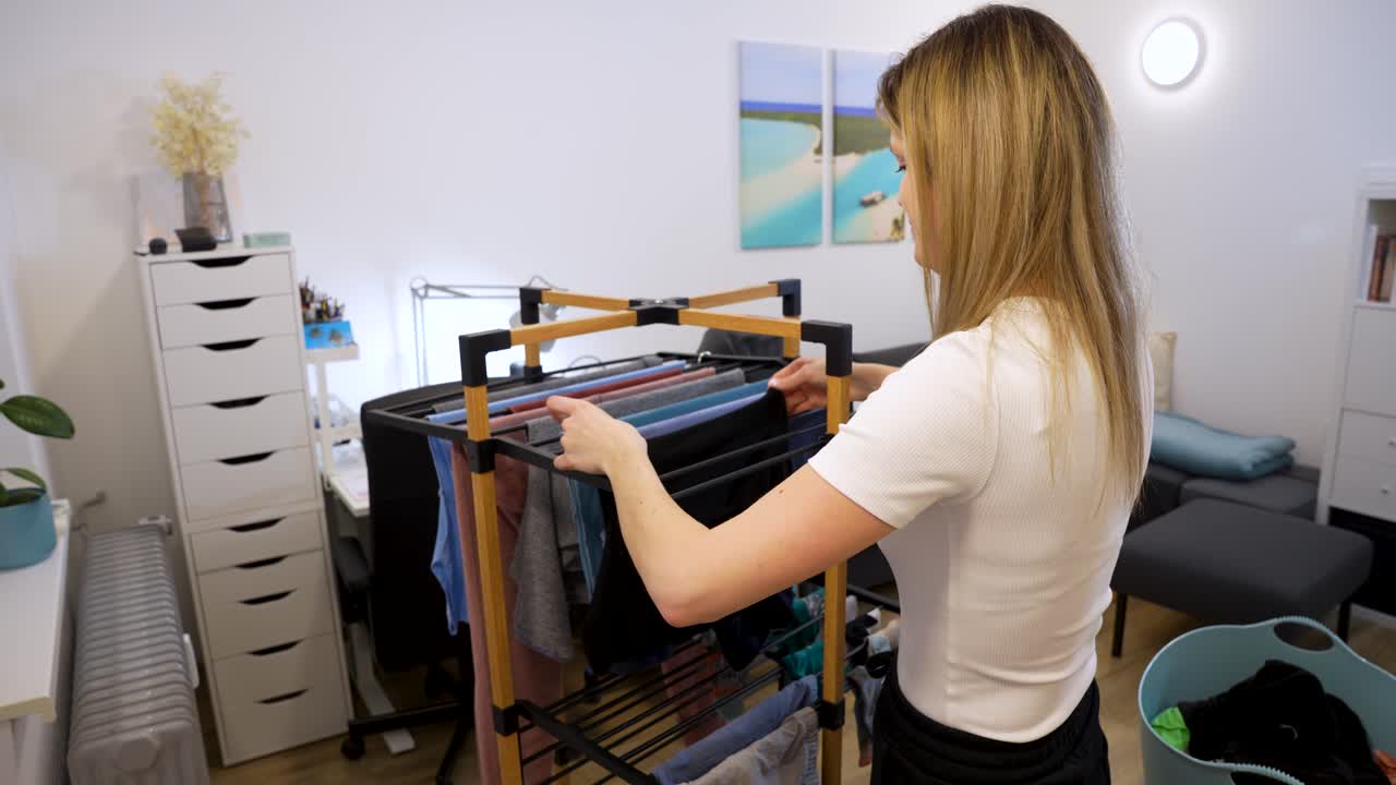 Home interior woman hanging washed clothes on drying rack after vacation, everyday laundry routine indoors