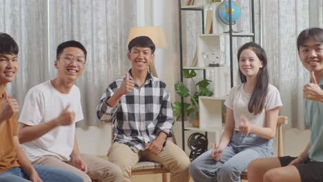 asian teen group sitting in chairs forming a circle discussing at home. smiling and showing thumbs up gesture to camera