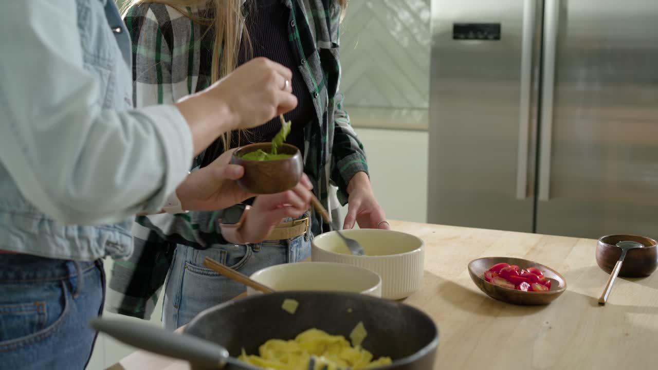 Due donne che prendono una pasta da una ciotola di legno su un'isola e dispongono le uova in ciotole bianche da condividere