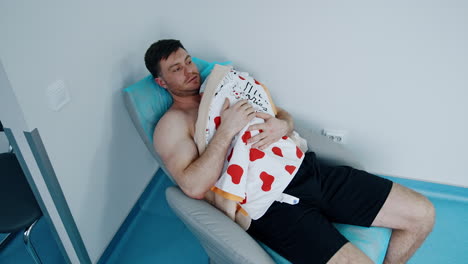happy caucasian male lies on the armchair holding his newborn child on the chest. skin-to-skin practice for a baby after c-section operation.