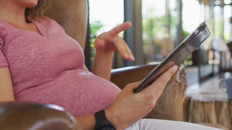 midsection of caucasian pregnant woman sitting in armchair using tablet