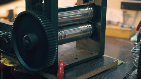 goldsmith forge-rolls metal with machine at table closeup