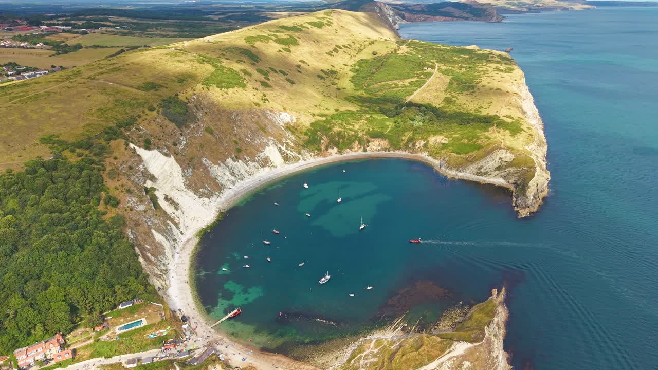 Circular drone view of boats in the turquoise water of Lulworth Cove in summer