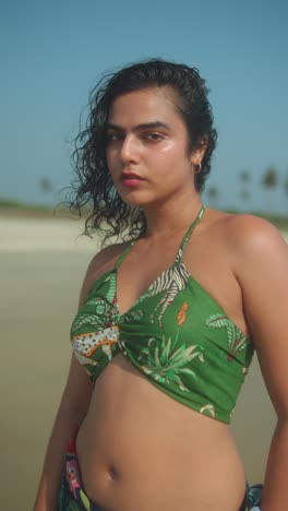 young woman in green bikini top standing confidently on tropical sunny beach