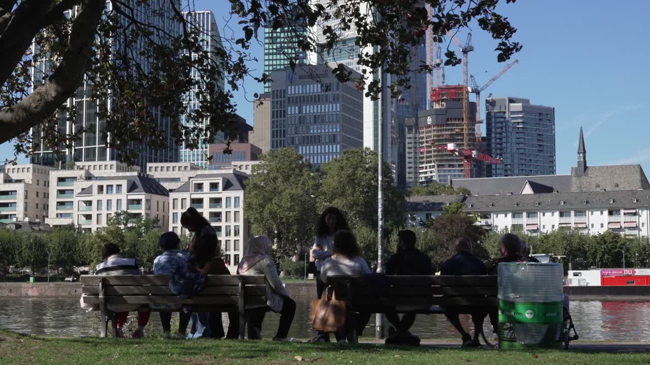 People relaxing on benches in a park with city skyline backdrop