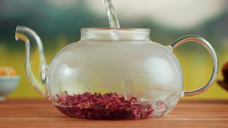 pouring hot water into a glass teapot to brew herbal tea
