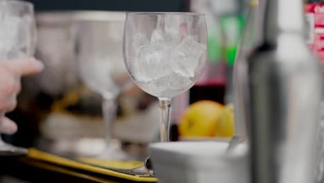 bartender preparing drinks, ice-filled glasses lined up on a bar counter, close up shot.