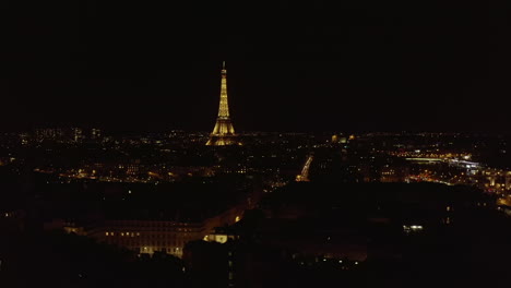 Forwards-fly-above-city-centre-at-night.-Illuminated-tall-landmark-towering-above-other-town-development.-Paris,-France