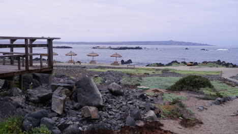 Panorámica-A-Través-De-Rústicas-Sombrillas-De-Playa-Vacías-En-La-Remota-Costa-Del-Océano-Chileno