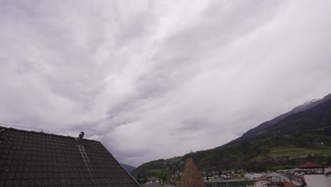 Timelapse-De-Nubes-En-Ciudad-Italiana-Con-Montañas,-Moviéndose-Hacia-La-Oscuridad