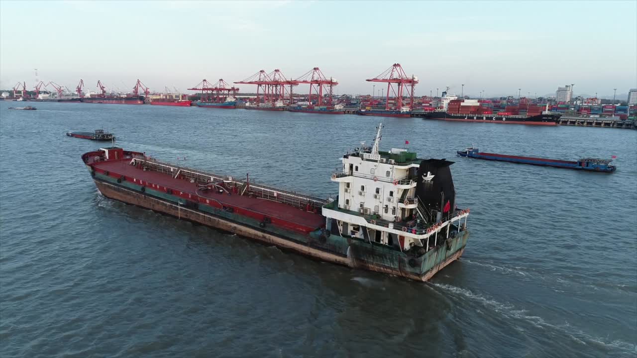 A cargo ship sailing in the sea, with container clusters at the port in the distance