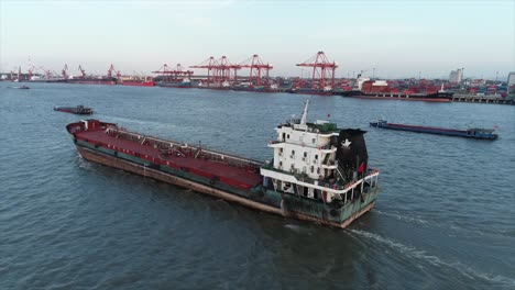 a cargo ship sailing in the sea, with container clusters at the port in the distance