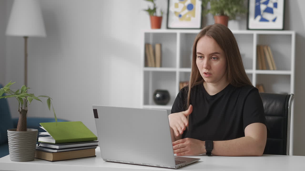 woman is conducting webinar sitting at home in front of laptop with web camera talking and gesticulating explaining and teaching medium portrait indoor