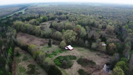 flying away from red barn in forestry area. high angle drone view