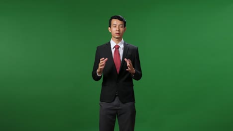 young asian businessman in suit jacket standing and presenting something on green screen background