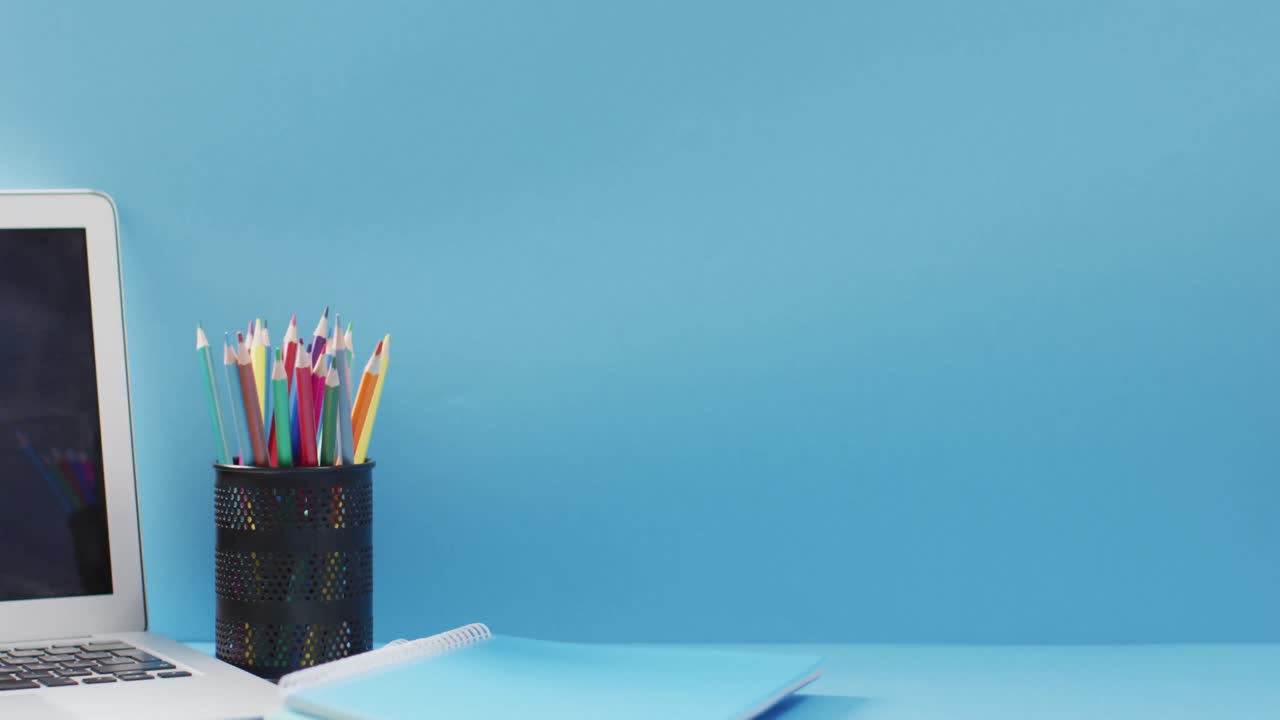 Video of cup with crayons and laptop in wooden table over blue background