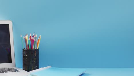 Video-of-cup-with-crayons-and-laptop-in-wooden-table-over-blue-background