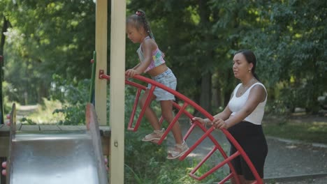 madre embarazada viendo a su hija jugar en el tobogán en el patio de recreo