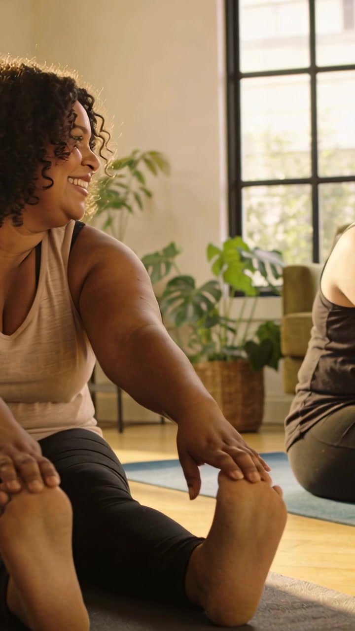 Vídeo vertical: Mulher de regata e leggings iniciando alongamento, tocando os dedos dos pés em tapete de yoga em aula