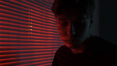 man looking through red blinds at night