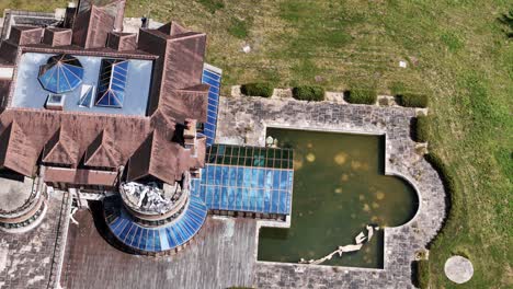 Unfinished celebrity mansion aerial view passing glass rooftop property, pool and landscaped gardens