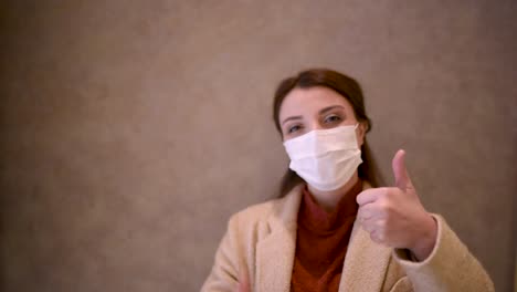 beautiful girl wearing protective medical mask and fashionable clothes does thumbs up gesture