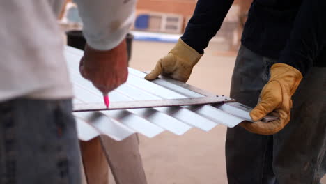 Construction-workers-on-a-crew-measuring-sheet-metal-with-a-straight-edge-ruler-and-marker-before-cutting