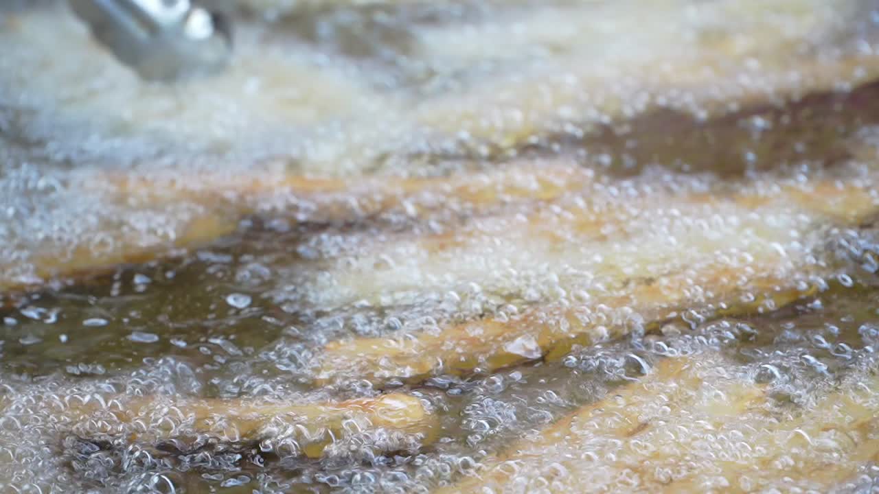 Closeup of a kitchen clamp turning churros being cooked in boiling oil.