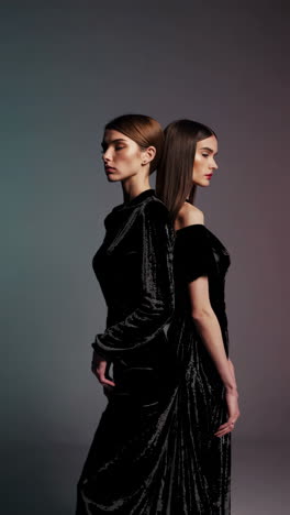 two women in elegant black velvet dresses standing back-to-back