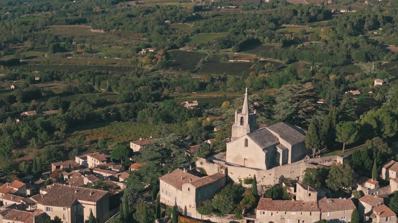 Panoramica aerea circolare a sinistra verso l'alto di Bonnieux, Francia, con chiese in cima alla collina, vigneti e montagne.