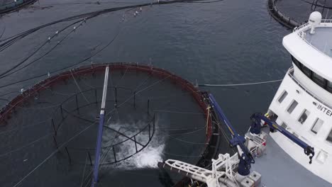 reversing drone shot of a well-boat placing fish in a fish farming cage