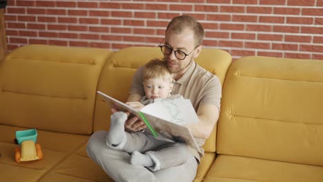 Father-reading-book-aloud-to-cute-son-at-home