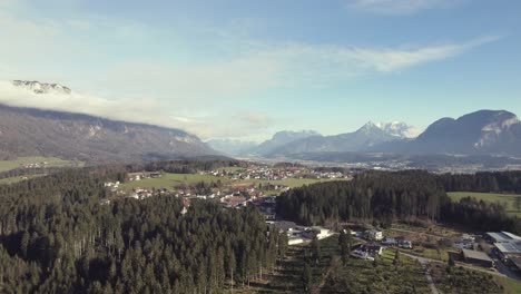Aerial-drone-of-beautiful-alpine-mountain-range-in-the-distance-with-grassy-fields,-trees-and-a-town