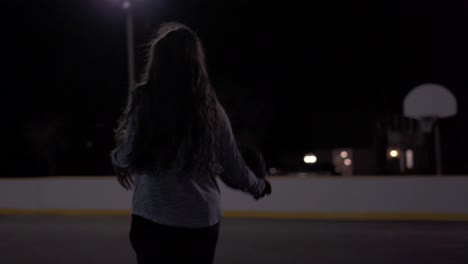 low angle tight shot of teenage girl dribbling basketball then taking a shot at an outdoor court at night with lights