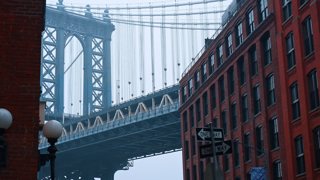 Ponte de Manhattan entre prédios de tijolos no bairro DUMBO. Vista da Ponte de Manhattan emoldurada por armazéns de tijolos vermelhos em DUMBO, no Brooklyn, em um dia de neblina