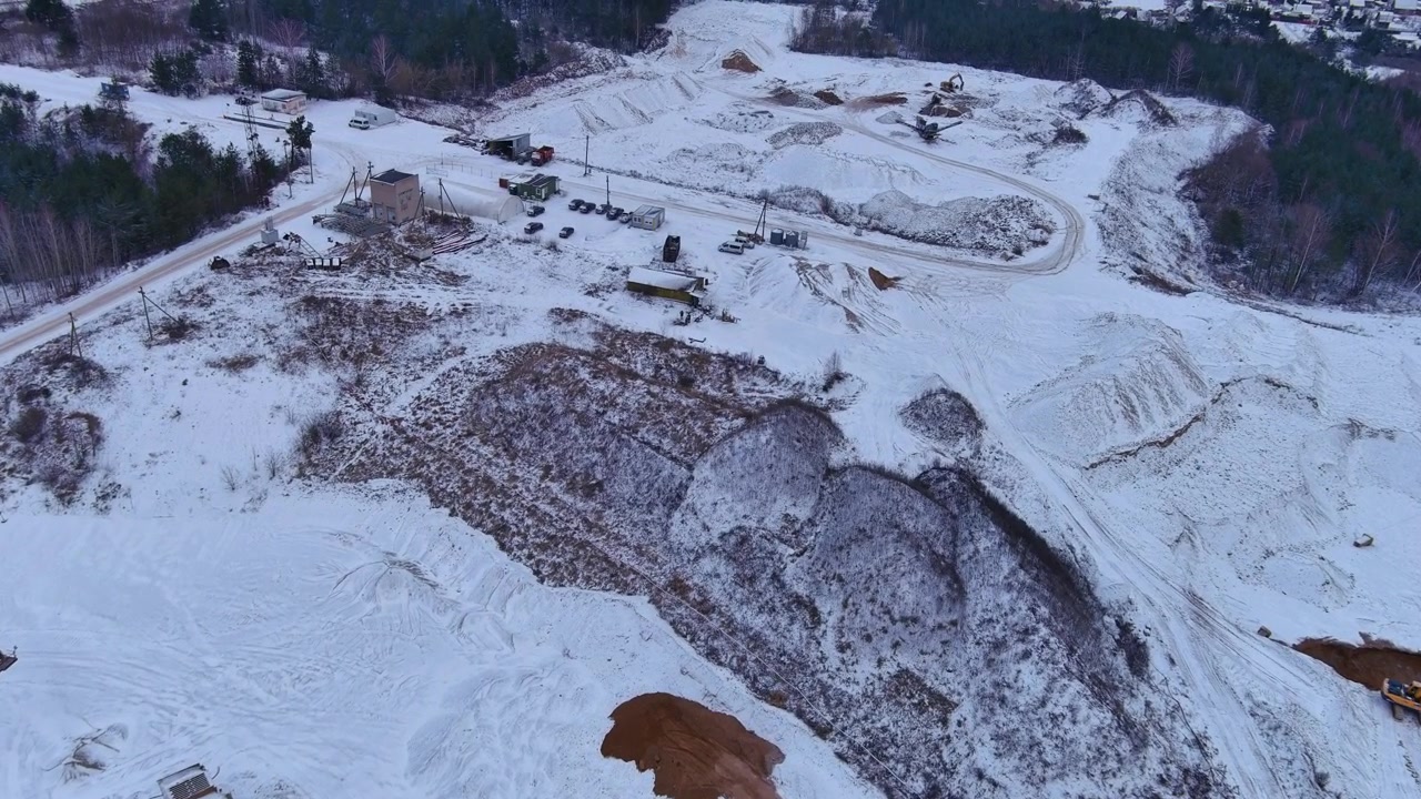 Draseikiain louhos lumen peitossa, esitellen dolomiitin louhintaa raskailla koneilla ja kuorma-autoilla. Kuva korostaa teollisuuden vaikutusta Liettuan talvimaisemaan. Dronen ilmakuva.