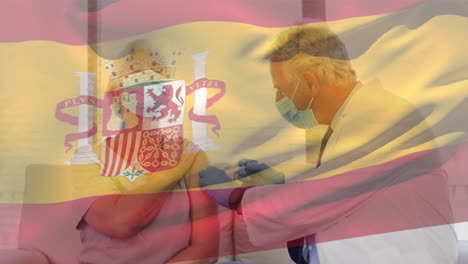 animation of flag of spain waving over doctor wearing face mask and vaccinating senior woman