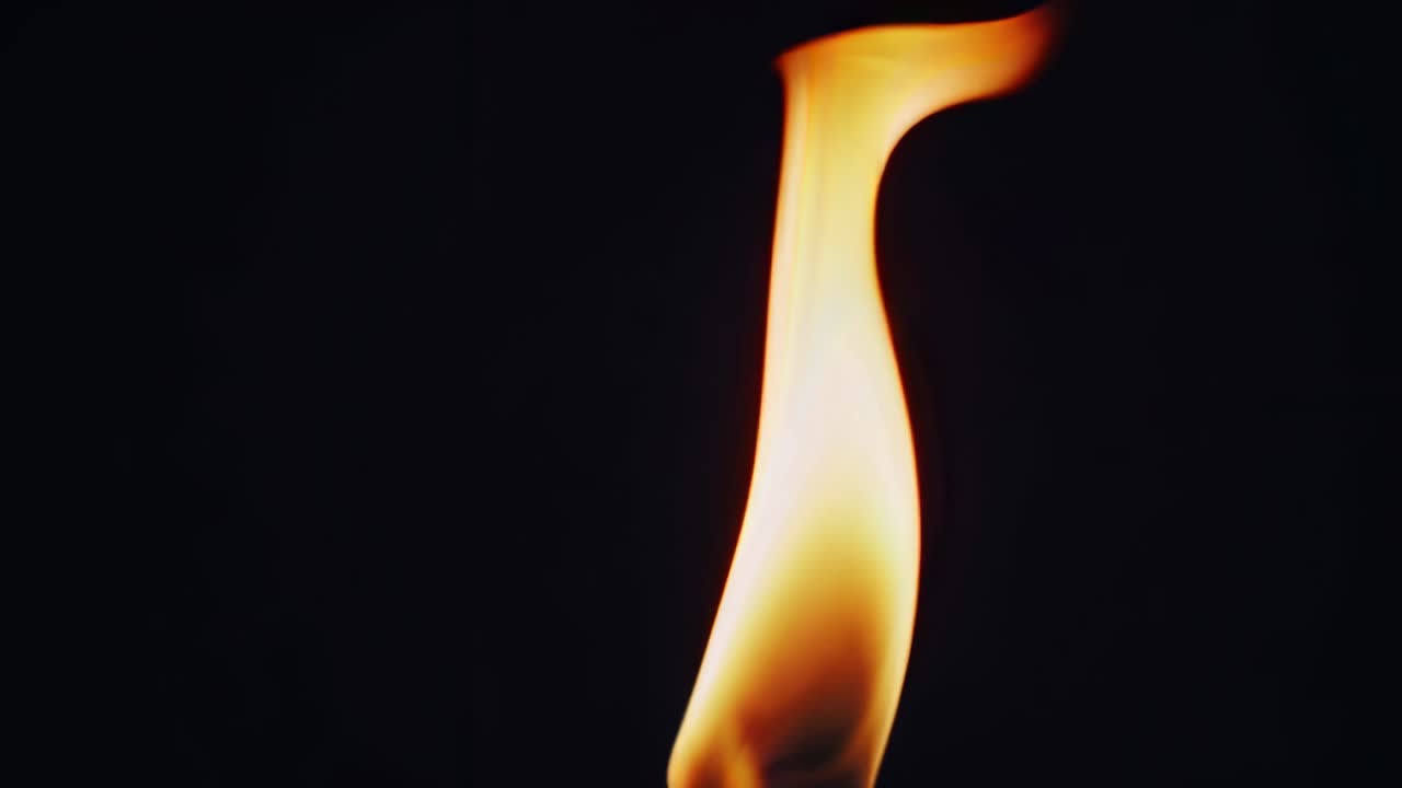 Close-up video of a flickering flame against a dark background, captured from a side angle