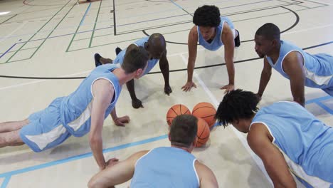 diverse male basketball team training, doing press ups in a circle at indoor court, slow motion