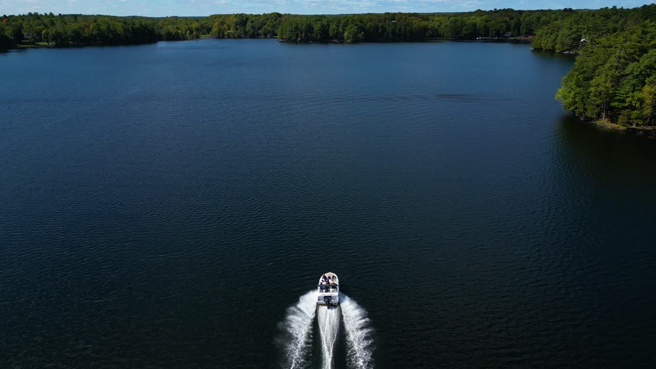 Drohnenaufnahme von oben von einem einsamen Boot, das eine helle Kielwasserlinie durch dunkelblaues Seewasser zieht, Übersicht aus hohem Winkel, nach oben geneigt